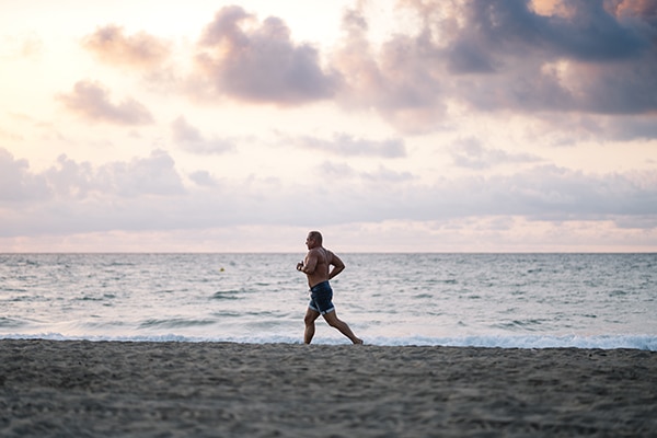 Strong old man makes exercise on the beach.