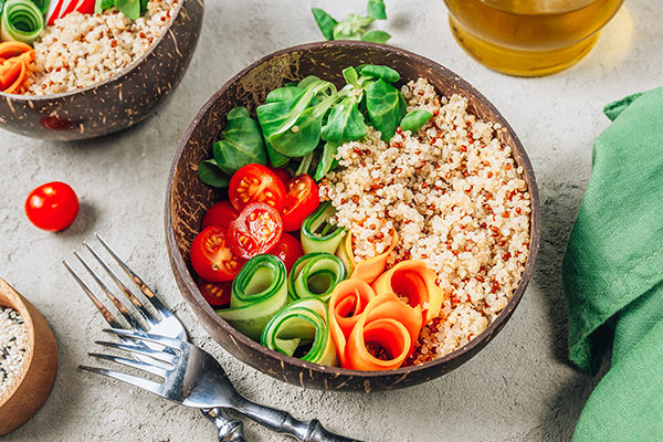 Vegan Buddha bowl. Healthy meal quinoa, tomato, cucumber, carrot, radish, corn salad in coconut bowls on concrete background. Selective focus