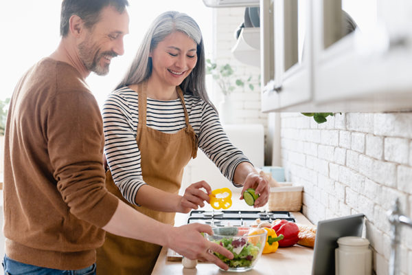 Happy mature middle-aged couple cooking vegetable vegetarian salad together in the kitchen