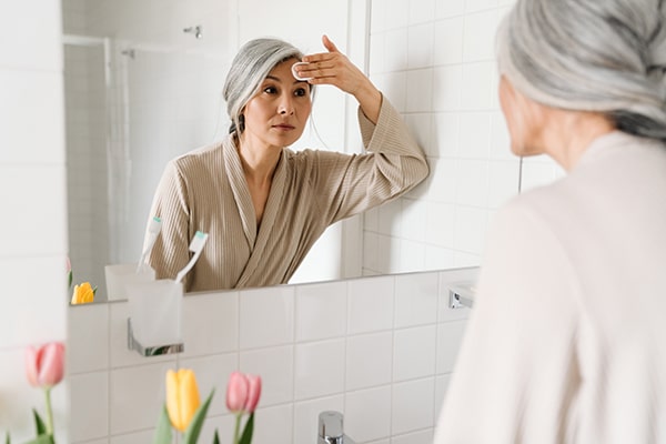 Mature grey woman cleaning her face with cotton pad in bathroom